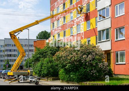 Apartment house facade maintenance works using modern self propelled telescopic boom lift with basket and hydraulic side outriggers Stock Photo