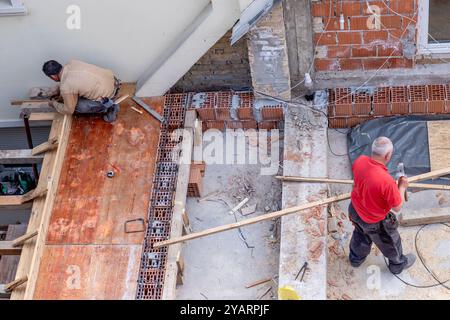 Construction workers are working on a wooden structure during the remodeling and extension of a residential house's rooftop. Stock Photo