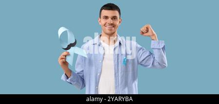 Young man with blue ribbon and paper mustache on blue background. Prostate cancer awareness concept Stock Photo