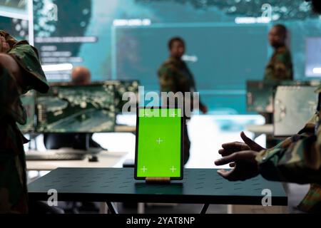 Two servicemen working together with an isolated copy space screen, using a tablet to help troopers in power base command post. Soldiers team examine real time information on device. Close up. Stock Photo