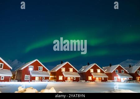 Northern lights over rorbu cabins in Svolvaer on Lofoten islands, Norway. Winter night with Aurora borealis, traditional red wooden houses, snowy moun Stock Photo