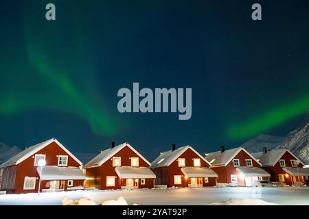 Northern lights over rorbu cabins in Svolvaer on Lofoten islands, Norway. Winter night with Aurora borealis, traditional red wooden houses, snowy moun Stock Photo