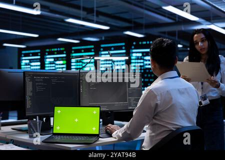 Teamworking technicians in server room using green screen laptop to find network issues affecting supercomputers. IT experts fixing slow data transfer rates in data center with chroma key notebook Stock Photo
