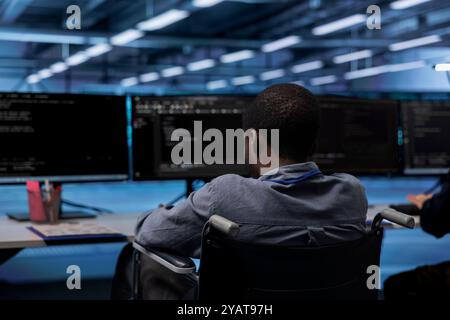 African american person with paraplegia working in inclusive server room workplace, typing on PC. Man in wheelchair doing tasks in data center housing advanced data storage infrastructure Stock Photo