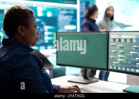 Woman governmental hacker analyzing digital threats on a computer, working in professional agency with a big screen. Specialist collecting information, fighting against cyberterrorism. Stock Photo