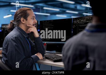 Admin in data center updating systems, protecting hardware equipment from damaging software vulnerabilities. Colleagues looking for bugs causing infrastructure to slow down Stock Photo