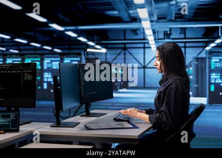 Programmer coding on PC, doing maintenance in data center to extend equipment life span and avoid downtime. Indian woman monitoring blade servers for overheating problems Stock Photo