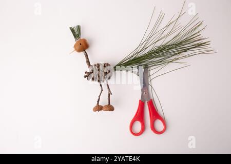 step in creative process, DIY, autumn craft, handmade bird crafted from pine cones and twigs, scissors cutting tail, fun activity for kids, Stock Photo