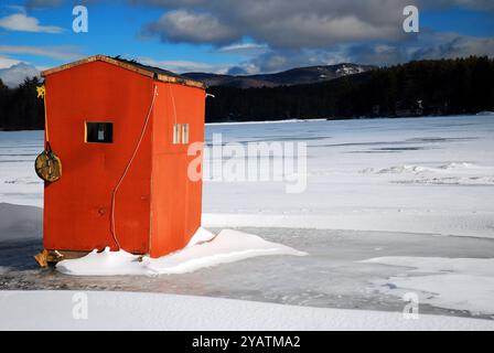 A lone ice fishing hut sits on a frozen lake on a winter day in New England Stock Photo