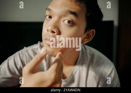 A man examining his facial hair while touching his chin, appearing thoughtful and focused Stock Photo