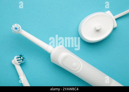 Modern electric toothbrush with spare heads and charger on blue background. Space for text Stock Photo