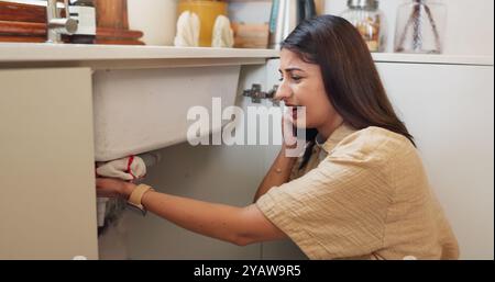 Woman, phone call or stress in kitchen for plumbing, booking consultation or cloth at sink. Homeowner, anxiety or talk on mobile for maintenance Stock Photo