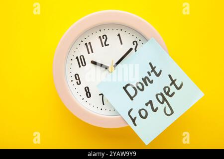 Alarm clock and reminder note with phrase Don't forget on yellow background. Top view Stock Photo