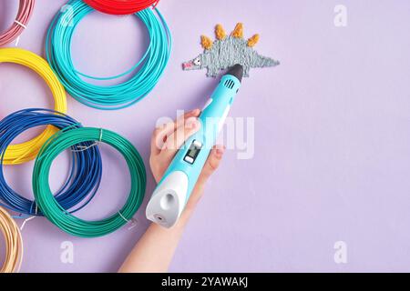 A hand holds a 3D pen and draws a dinosaur on a purple background. Perfect for projects related to crafts, technology, or DIY Stock Photo