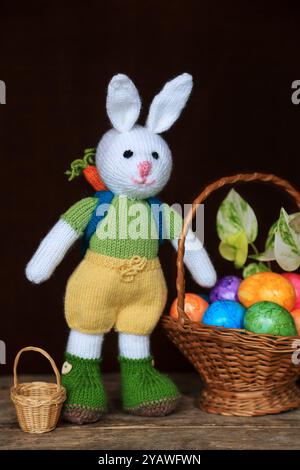 Knitted white rabbit with a rucksack standing with a basket of Easter eggs Stock Photo