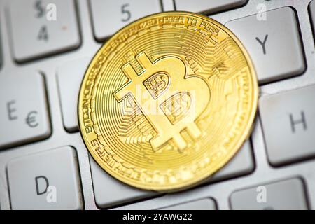 Bitcoin leaning against a computer keyboard on white background Stock Photo