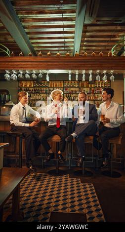 Cheerful group of men, smiling and drinking together, embodying joy and camaraderie of night out after busy work-day. Stock Photo