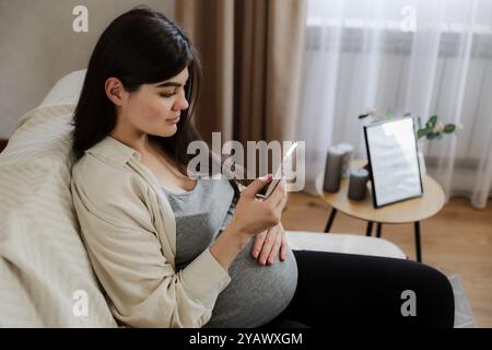 Beautiful pregnant woman with baby belly touch mobile cell phone. Close up, copy space. Busy pregnancy, tracking, communication concept. Order food, chatting on device, booking hotel, air ticket Stock Photo