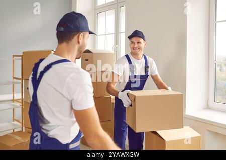 Cheerful employees of transportation and delivery company carry cardboard boxes together. Stock Photo