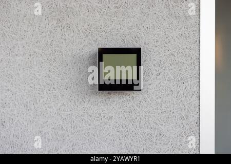 Electronic thermostat mounted on white wall displaying current indoor temperature. Device is sleek, modern, and essential for climate control in a minimalist environment. Stock Photo
