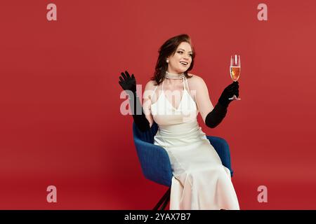 A young woman in a stunning gown joyfully raises a champagne glass against a striking backdrop. Stock Photo