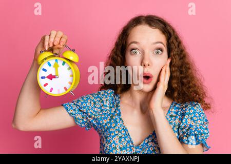 Surprised woman holding colorful alarm clock on pink background Stock Photo