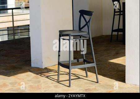 Bathed in sunlight, a sleek black bar stool occupies a spacious outdoor patio, inviting guests to relax and enjoy casual meals in a stylish environmen Stock Photo