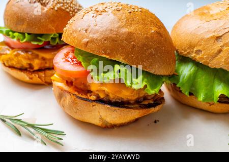 Juicy three burgers with beef patty, tomatoes, onions and lettuce on baking paper. on a light background. High quality photo Stock Photo