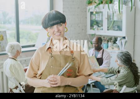 Portrait of young adult smiling drawing teacher holding paintbrushes and looking directly at camera Stock Photo