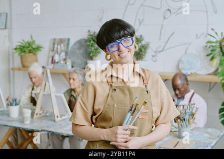 Portrait of young adult Caucasian drawing teacher holding paintbrushes and posing for photo Stock Photo