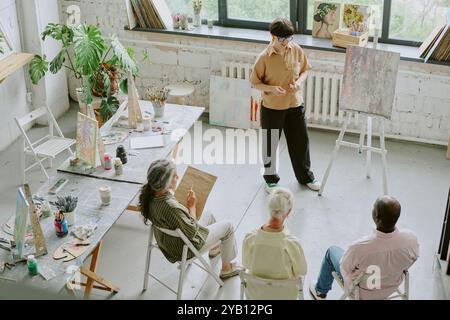 High angle shot of senior students listening to young talented drawing teacher while they sitting in chairs and taking notes Stock Photo