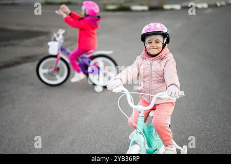 Two young children, dressed in warm clothing and helmets, happily ride their bicycles on an empty road during a winter day, showcasing joy and outdoor Stock Photo