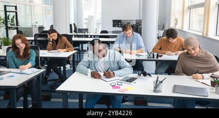 Diverse group of students sitting at desk writing in classroom Stock Photo