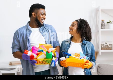 Big Cleaning Day. Smiling Black Couple Holding Containers With Household Tools Stock Photo