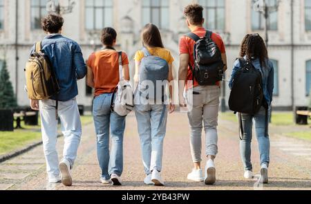 Group of five students with backpacks walking at university campus together Stock Photo