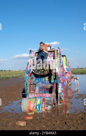 A man climbing on a Cadillac at Cadillac Ranch in Amarillo, Texas Stock Photo