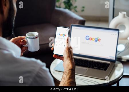 Businessman using Google search website in a mobile phone and a laptop too, to do an internet search. Rosario, Argentina - October 16, 2024. Stock Photo
