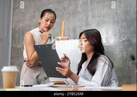 Two focused and professional Asian businesswomen are reviewing documents together and discussing them during the meeting. colleagues, teamwork, brains Stock Photo