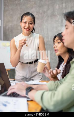A confident, attractive Asian businesswoman or female manger is in the meeting with her team members, smiling at the camera. Stock Photo