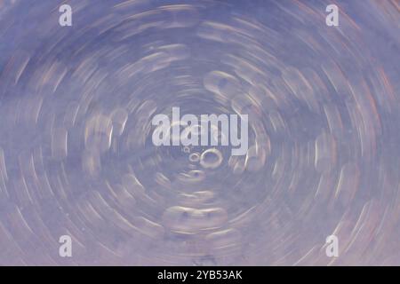 This macro photograph features an abstract background with swirling droplets that resemble a cosmic scene. Stock Photo