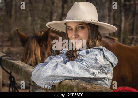 A beautiful brunette cowgirl poses with her horse before a ride in the countryside Stock Photo