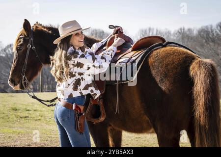 A beautiful brunette cowgirl poses with her horse before riding in the country Stock Photo