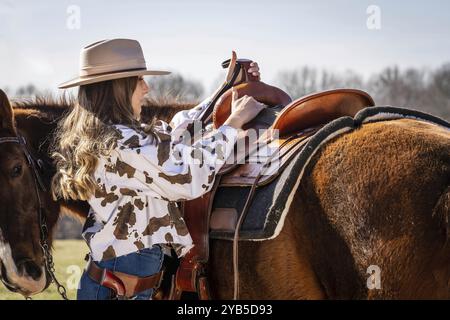 A beautiful brunette cowgirl poses with her horse before riding in the country Stock Photo