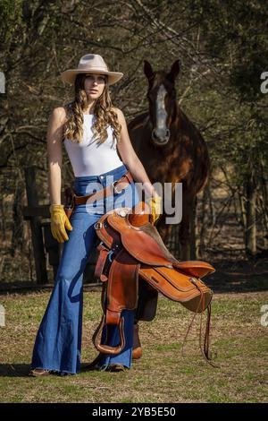 A beautiful brunette cowgirl poses with her horse before riding in the country Stock Photo