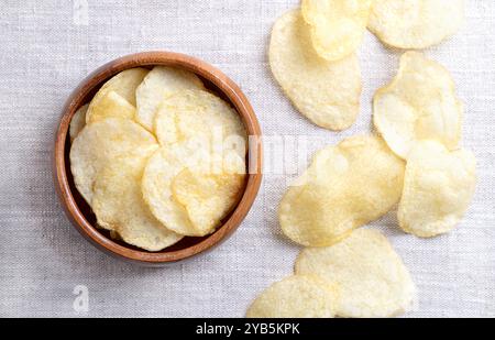 Salted potato chips in a wooden bowl on linen fabric. Fresh and ready to eat crisps, slim slices of deep fried potato. Stock Photo