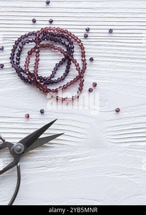 Colorful beads and scissors are arranged on a white wooden tabletop, highlighting a creative activity focused on beading or jewelry making. Stock Photo