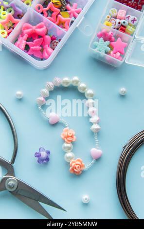 A creative workspace displays vibrant beads and charms, with a nearly finished bracelet adorned with flowers and hearts. Tools are arranged for crafti Stock Photo