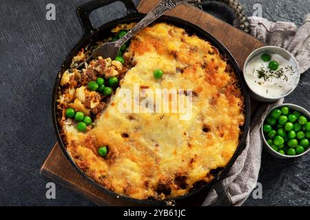 Shepherd's Pie with ground beef, potato and cheese on black background, top view. Traditional homemade potato casserole with green pea. Stock Photo