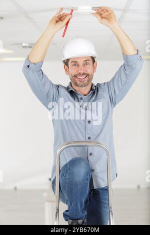 man using screwdriver to install smoke detector on ceiling Stock Photo