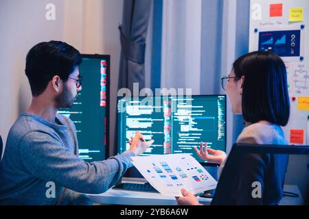 Asian software developers teams working on multiple screens displaying code and application diagrams at night in modern office Stock Photo